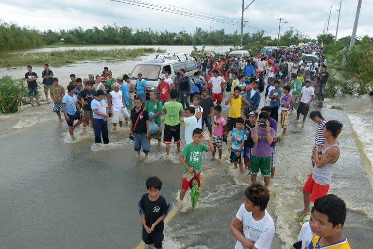 Stranded people stand as vehicles maneuver though flood waters after Typhoon Nari swept across the northern Philippines, on October 12, 2013