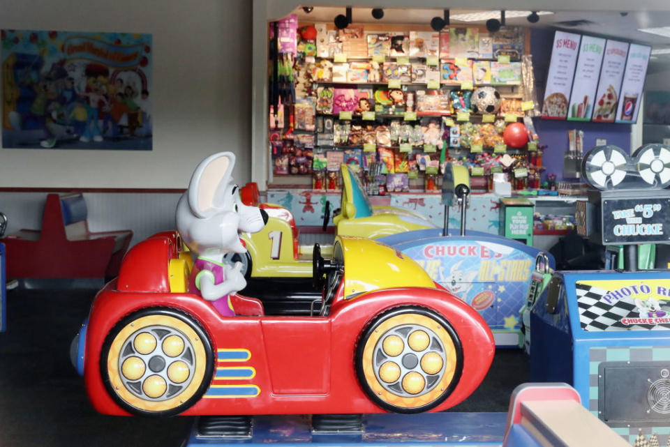 Chuck E. Cheese mascot statue in a red car inside the play area, surrounded by arcade games and prize counter