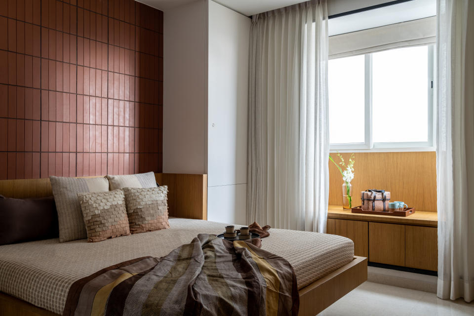 Bedroom with terracotta tiled wall behind bed, wooden window seat and neutral soft furnishings