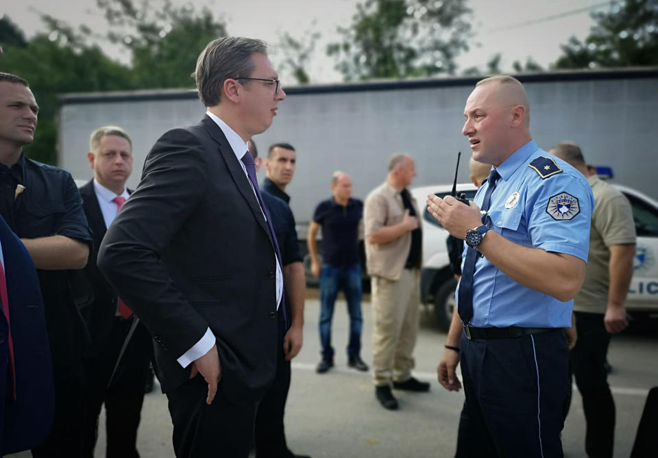 In this photograph made available by the Serbian Presidency, a Kosovo police officer speaks to Serbia's president Aleksandar Vucic, left, to say he cannot continue his trip to the village of Banje due to roadblocks, in Zubin Potok, Kosovo, Sunday, Sept. 9, 2018. Kosovo Albanians burned tires and blocked roads with wooden logs, trucks and heavy machinery on a planned route by Serbia's president who is visiting Serbs in the former Serbian province.(Serbian Presidency via AP)