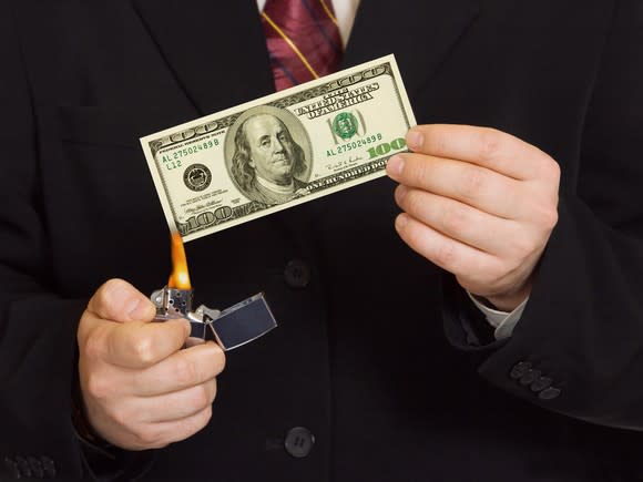 A person in a suit lighting a 100 dollar bill on fire.