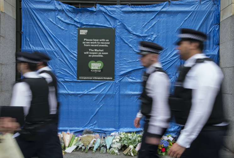 Police officers walk past floral tributes in Borough Market after the attack (Picture: PA)