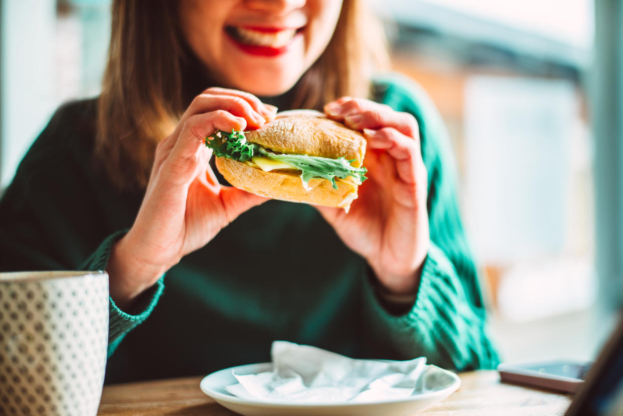 Cheerful businesswoman enjoying a freshly made fibre veggie burger while having lunch break with colleague in cafe.