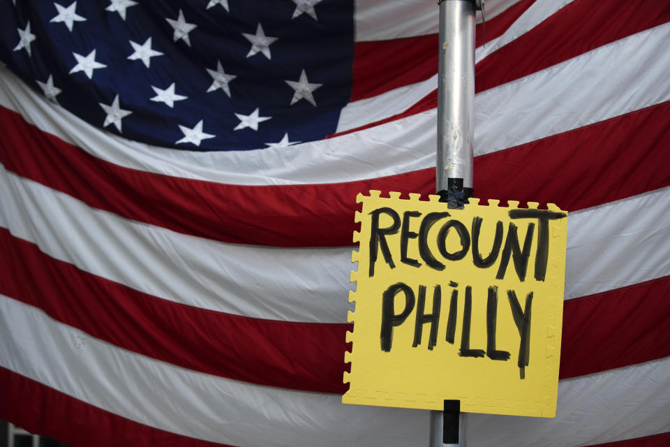 A sign hangs in front of an American flag, as a handful of supporters of President Donald Trump continue to protest outside the Pennsylvania Convention Center, in Philadelphia, Tuesday, Nov. 10, 2020. (AP Photo/Rebecca Blackwell)