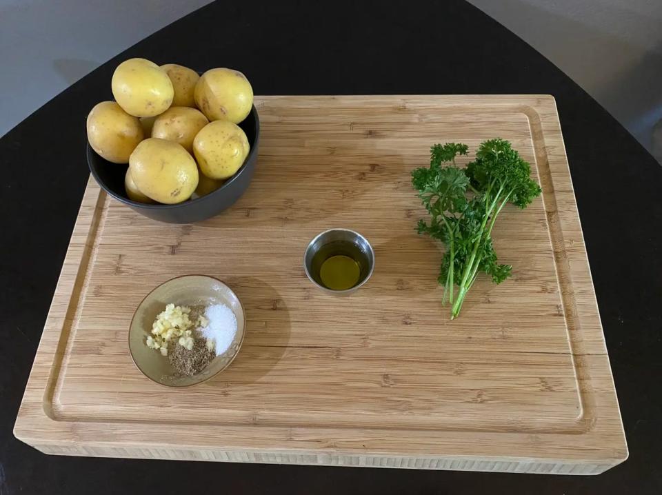 potatoes, garlic, seasonings, oil, and herbs on a wooden cutting board