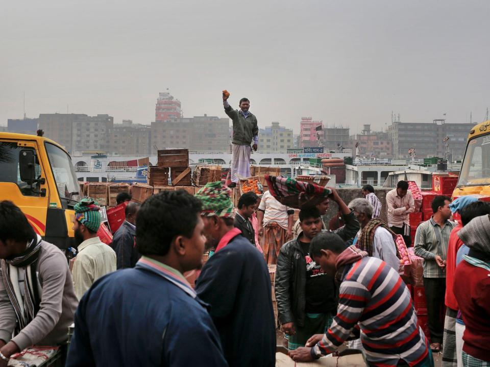 A manA Bangladeshi roadside vendor, standing on a pile of boxes, shouts out to passersby holding fruits in his hand to attract their attention on an overcast day on the banks of the River Buriganga in Dhaka, Bangladesh, Thursday, Jan. 21, 2016.