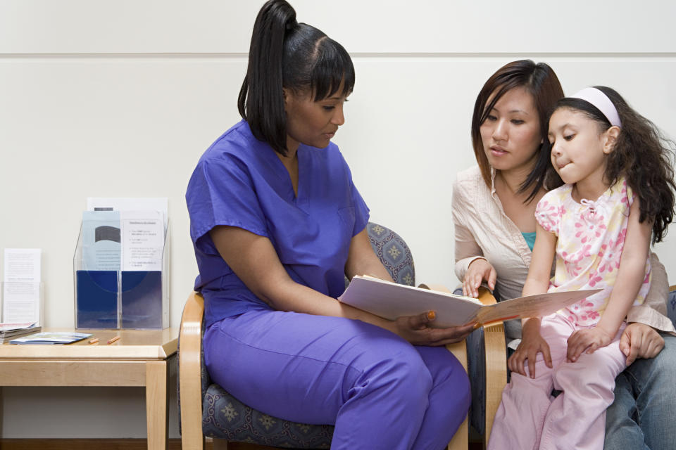 A nurse shows a document to a woman and child seated beside her