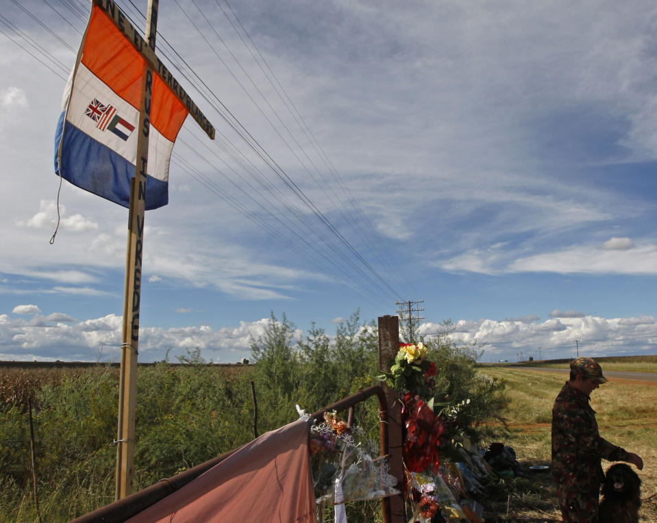 FILE -- In this Wednesday, April 7, 2010 file photo a guard and his dog provides outside slain white supremacist leader Eugene Terreblanche's farm in Ventersdorp, South Africa beneath an old South African flag. South Africa's Equality Court has restricted the display of the old apartheid-era flag in a ruling issued Wednesday Aug. 21, 2019, that it's gratuitous use amounts to hate speech and racial discrimination. (AP Photo/Schalk van Zuydam)