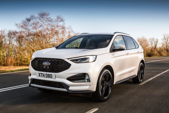 A white 2019 Ford Edge, a midsize SUV, with UK license plate, on a country road.