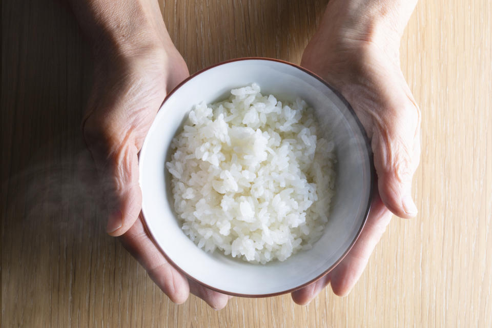 Two hands holding a white bowl of steamed rice