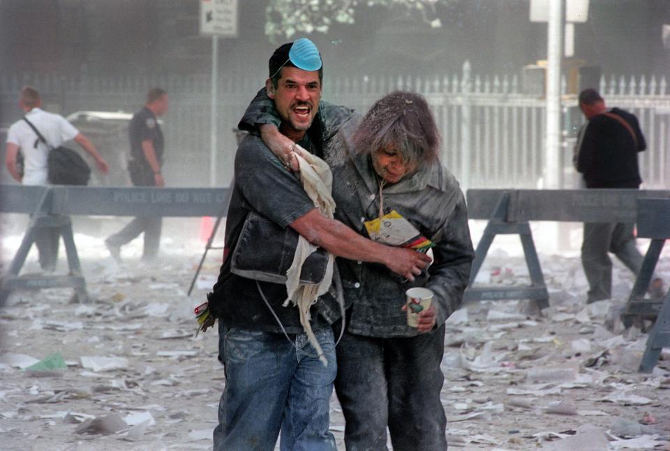 A man supports a woman as they walk through the rubble on 9/11.