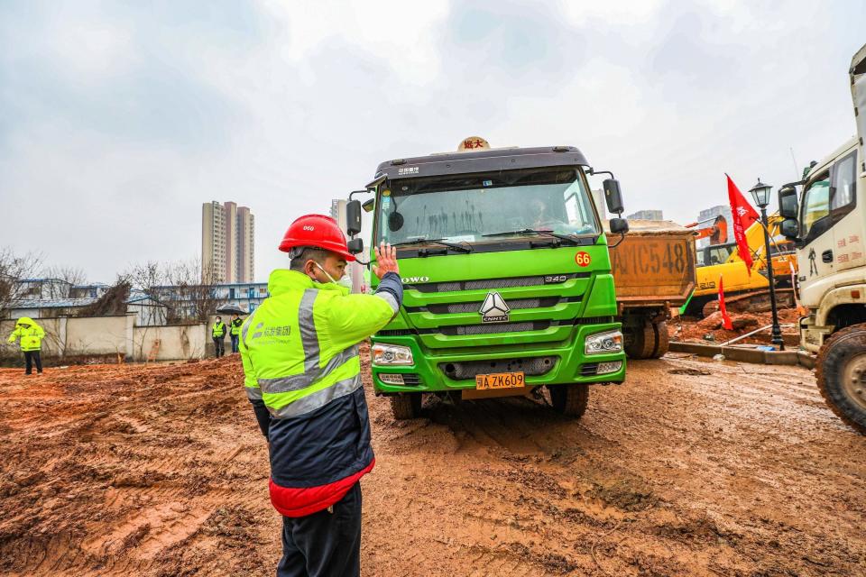 A worker controls the flow of trucks entering the site.