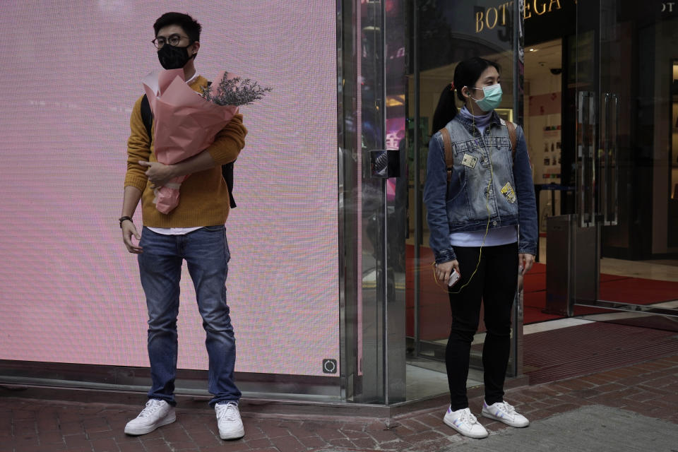 A man wearing protective face mask waits at a street corner with a bouquet on Valentine's Day in Hong Kong, Friday, Feb. 14, 2020. China on Friday reported another sharp rise in the number of people infected with a new virus, as the death toll neared 1,400. (AP Photo/Kin Cheung)