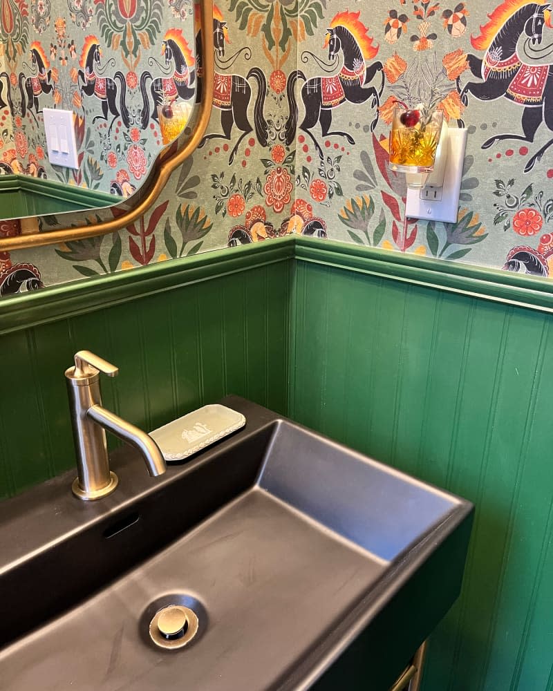 bathroom sink area with green wainscoting, horse wallpaper, large basin sink, and gold mirror after makeover