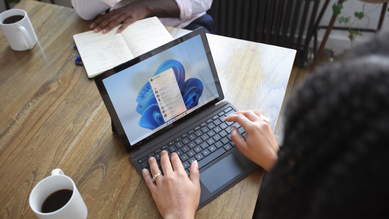  A woman at a table using a Windows laptop, opposite sits a man, neither show their face. 