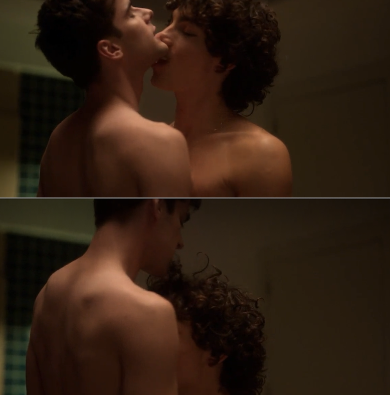 Two shirtless individuals, one with short hair and the other with curly hair, are embracing intimately in a dimly lit room