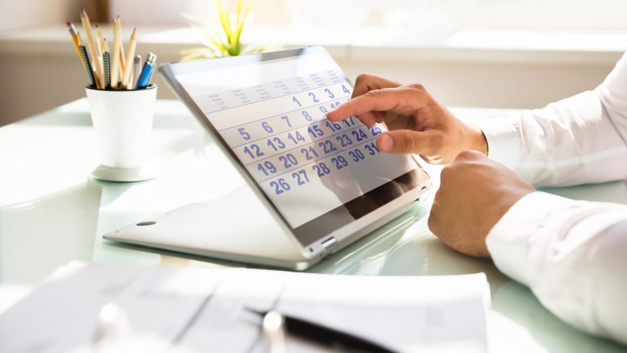 Close-up of a businessman's hand using calendar on laptop over desk.