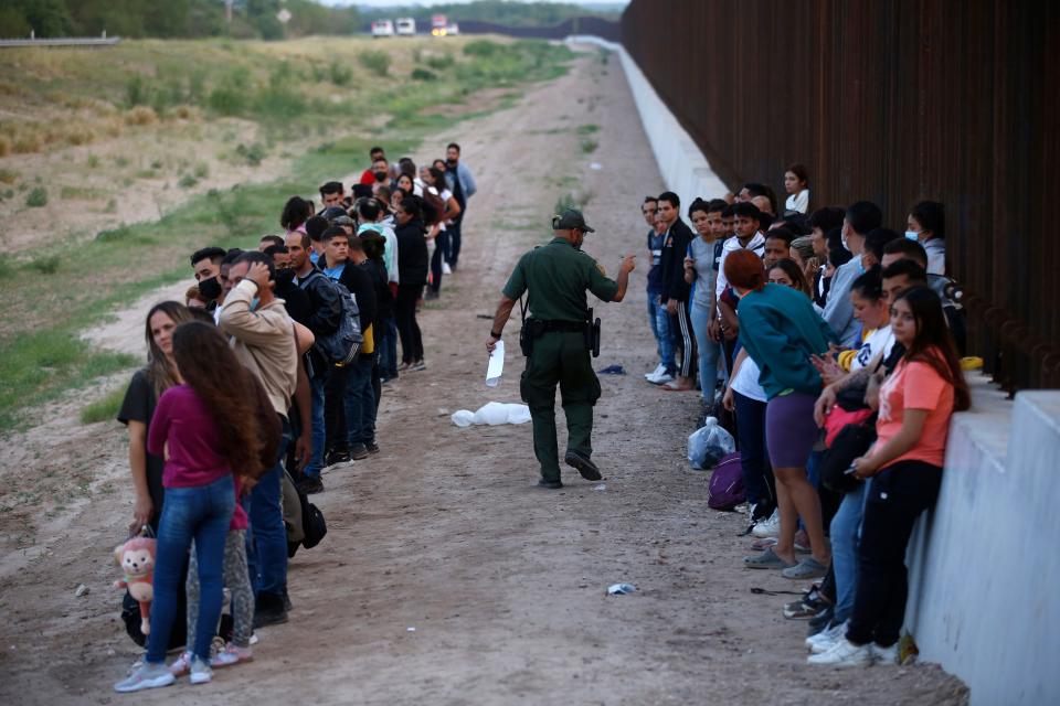 Migrants stand next to the border wall as a Border Patrol agent takes a head count in Eagle Pass on May 21.