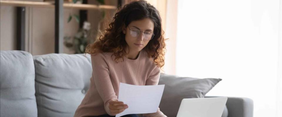 Focused young woman in glasses sits on couch looking at piece of paper