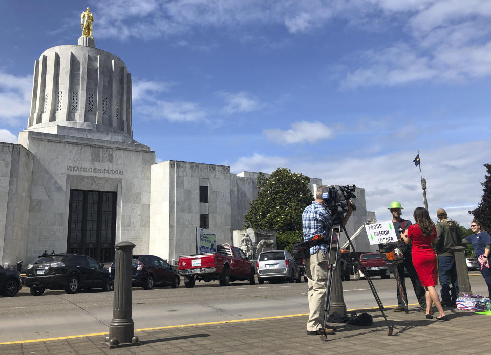 A TV reporter interviews self-employed logger Bridger Hasbrouck, of Dallas, Ore., outside the Oregon State House in Salem, Ore., on Thursday, June 20, 2019, the day the Senate is scheduled to take up a bill that would create the nation's second cap-and-trade program to curb carbon emissions. Senate Republicans, however, pledged to walk out so there wouldn't be enough lawmakers present for a vote on House Bill 2020, which is extremely unpopular among loggers, truckers and many rural voters. (AP Photo/Gillian Flaccus)