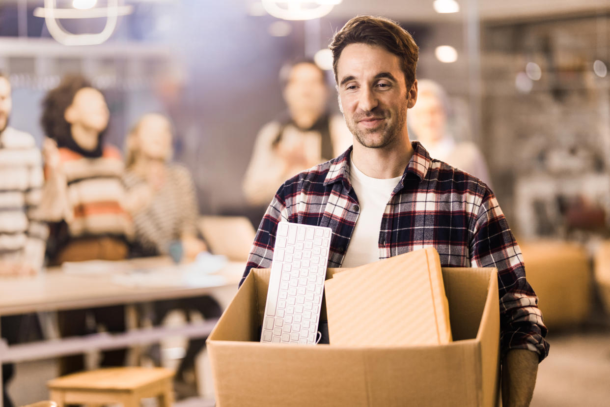 Happy male entrepreneur quit his job and leaving the office satisfied. There are people in the background.