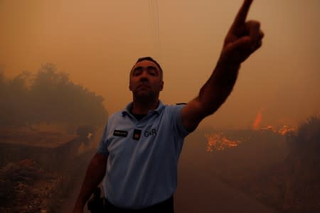 A police officer blocks the journalists next to a fire at the small village of Colos