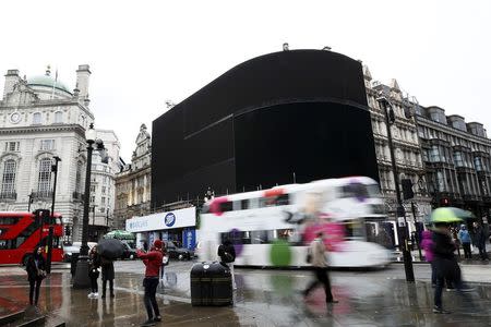 People walk past the advertisement boards at Piccadilly Circus which have been switched off prior to being replaced with more modern screens, in central London, Britain January 16, 2017. REUTERS/Stefan Wermuth,