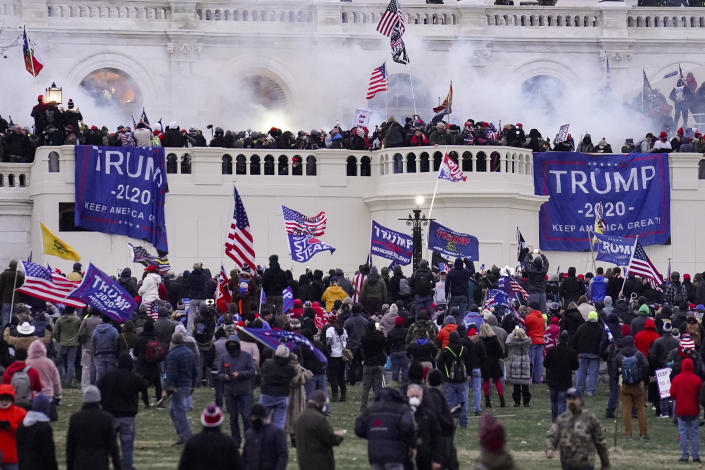 Rioters storm the Capitol in Washington, with clouds of teargas on the balcony among the American flags. 