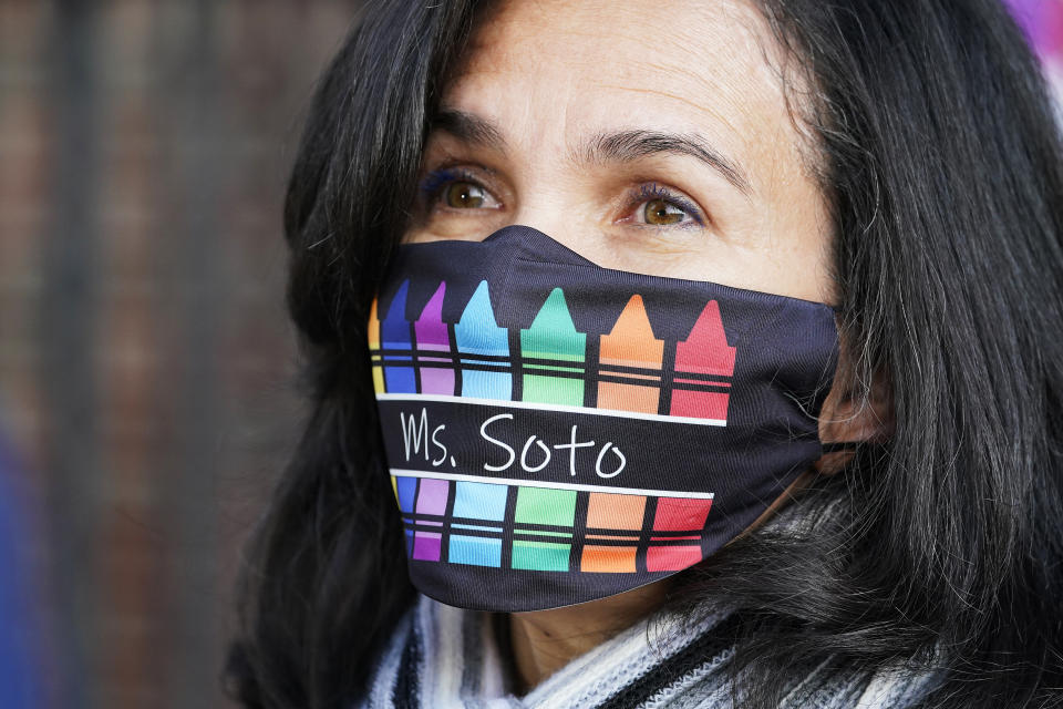 Homeris Soto, a para-professional with Mosaic Pre-K Center, wears a mask decorated with crayons as she greets students for the first day of school, Monday, Sept. 21, 2020, in New York. The city public schools delayed reopening for two weeks. (AP Photo/Mark Lennihan)