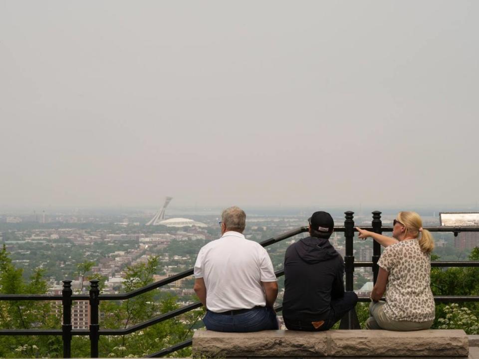 A group of tourists look east from a lookout on Mount Royal on Monday. A smog warning is in effect for Montreal and multiple regions of the province due to forest fires. (Christinne Muschi/The Canadian Press - image credit)