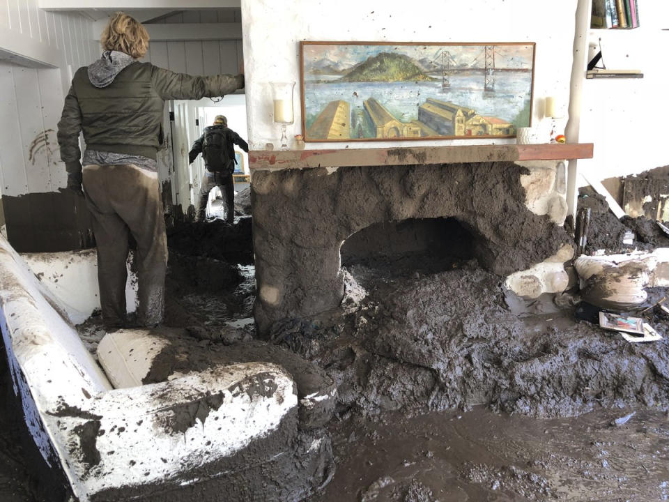 <p>Teresa Drenick stands in her sister’s home damaged after heavy rains off Glen Oaks Lane, while Sean Bornwell retrieves some of her sister’s personal belongings on Wednesday, Jan. 10, 2018, in Montecito, Calif. Drenick’s sister has been missing since early Tuesday morning. (Photo: Mike Eliason/Santa Barbara County Fire Department via AP) </p>