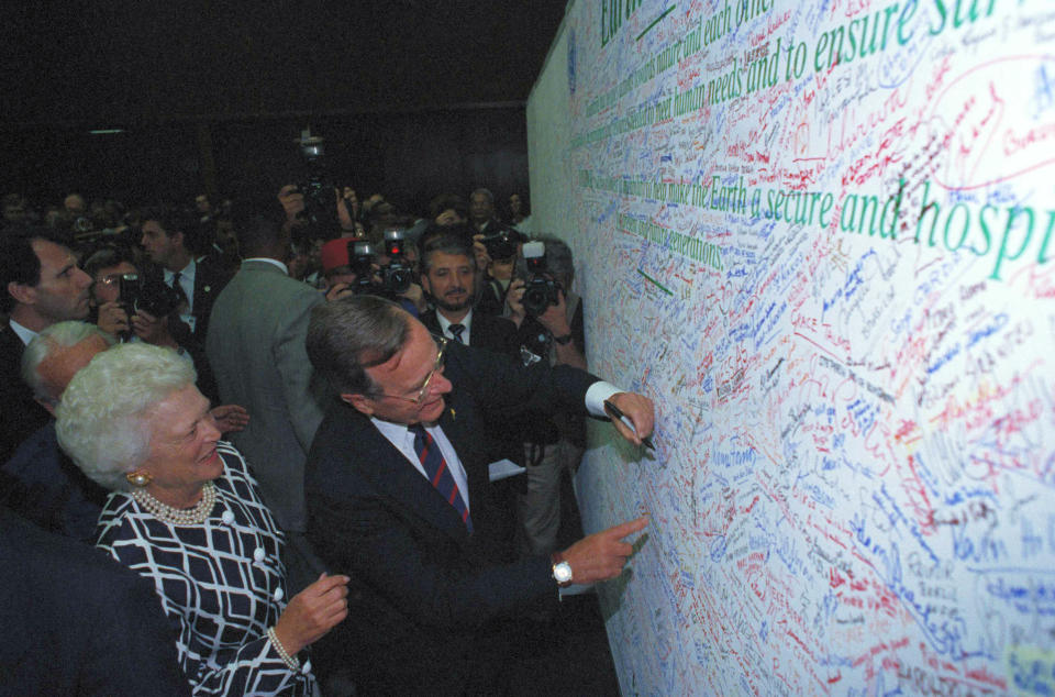 FILE - U.S. President George Bush is watched by first lady Barbara Bush as he signs the Earth Pledge at the Earth Summit in Rio de Janeiro, June 12, 1992. The Earth Pledge says that each signer pledges to work to the best of his or her ability to protect the earth. (AP Photo/M. Frustino)