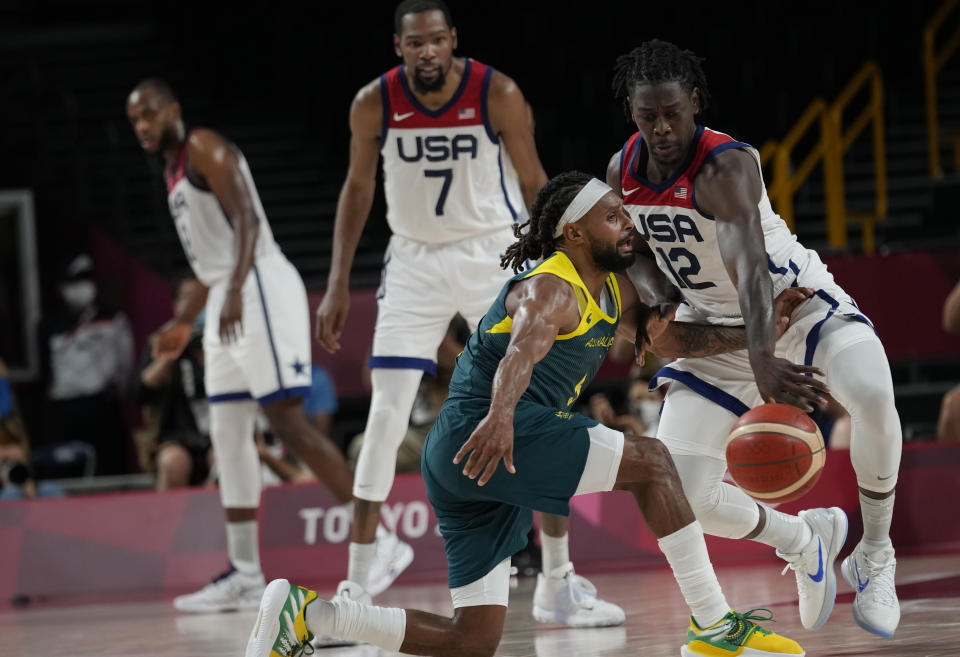 United States's Jrue Holiday (12), right, knocks the ball away from Australia's Patty Mills (5), front, during men's basketball semifinal game at the 2020 Summer Olympics, Thursday, Aug. 5, 2021, in Saitama, Japan. (AP Photo/Eric Gay)