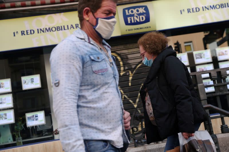 FILE PHOTO: People wearing protective face masks walk past a real estate agency during the coronavirus disease (COVID-19) outbreak in Madrid