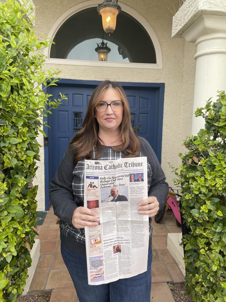 Nicole Leonardi, holds a copy of the "Arizona Catholic Tribune" at her home in Tempe, Ariz. on Thursday, Nov. 2, 2022. The paper is part of a multi-state network of partisan conservative online and print publications that give the appearance of a traditional local media outlets. (AP Photo/Josh Kelety)