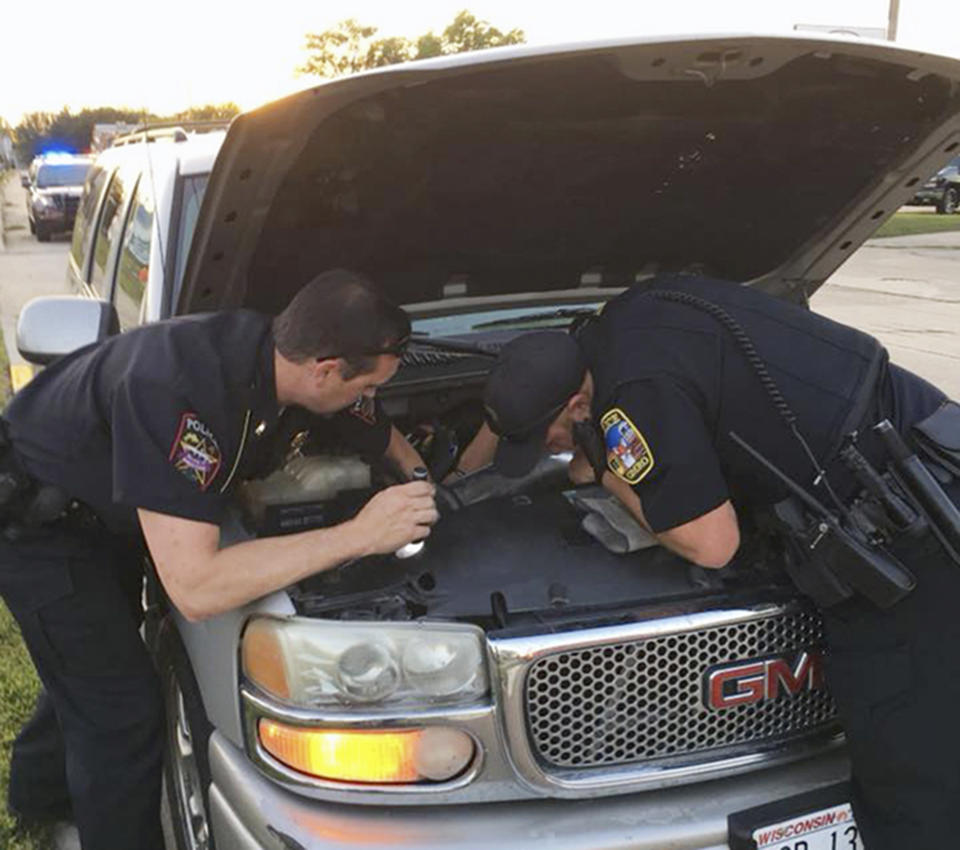 This Wednesday, Aug. 22, 2018, photo provided by the Omro Police Department in Omro, Wis., shows police officers trying to remove a 4-foot-long Ball python that was discovered wrapped around a car engine. It took hours to unwind and coax the snake from the engine compartment. Police say the snake escaped from its owner more than a month ago. (Omro Police Department via AP)