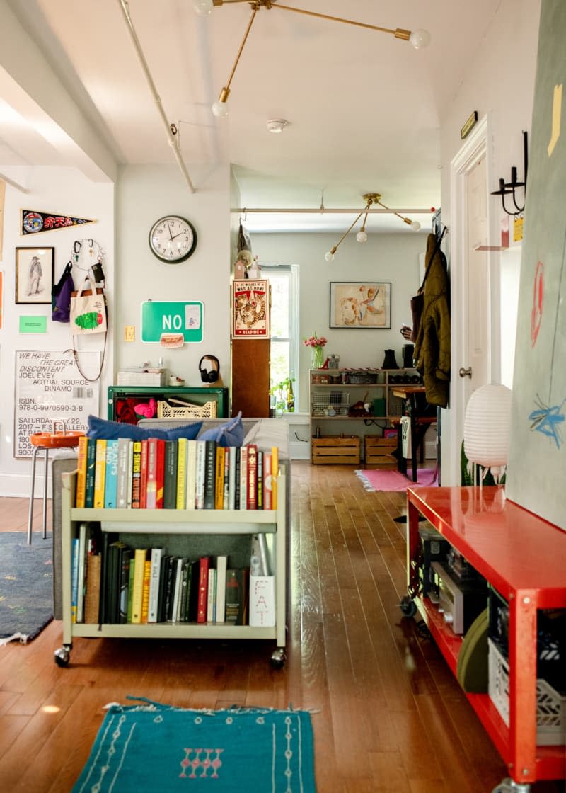 Living room with rolling bookcase across from wall-sized piece of art.