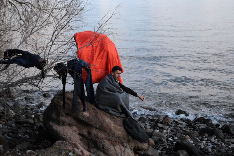 A migrant, who arrived the previous day on a dinghy after crossing part of the Aegean Sea from Turkey, is covered with a blanket while sitting on a rock near the village of Skala Sikamias, on the island of Lesbos