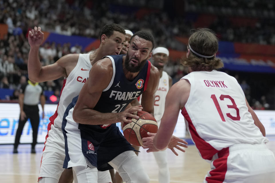 France center Rudy Gobert (27) passes around Canada forward Kelly Olynyk (13) during the Basketball World Cup group H match between France and Canada at the Indonesia Arena stadium in Jakarta, Indonesia, Friday, Aug. 25, 2023. (AP Photo/Dita Alangkara)