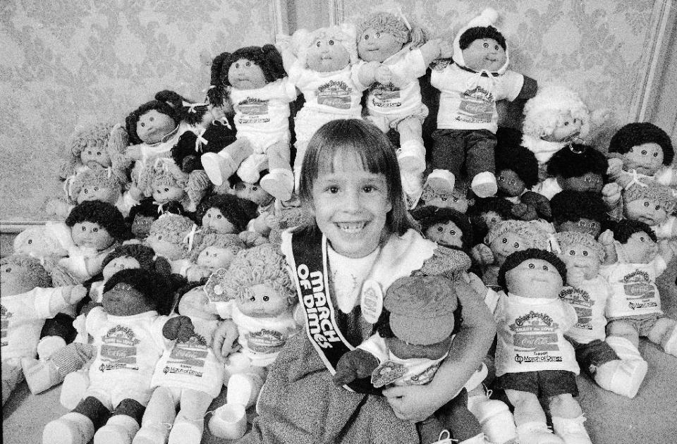 FILE - In this Aug. 30, 1984, file photo, Helen Humphrey, the 1984 National Poster Child for the March of Dimes Birth Defects Foundation, smiles as she holds Cabbage Patch Kids in New York. Created in 1978, plush Cabbage Patch Kids with yarn hair became one of the biggest toy crazes in the 1980s. (AP Photo)