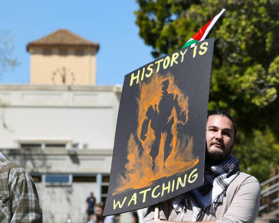 Brooks Martin, a Cal Poly grad student, holds a sign that reads “History is watching” as about 70 people gathered on Cal Poly’s Dexter Lawn on May 1, 2024, to stage a silent die-in in support of Palestine. David Middlecamp/dmiddlecamp@thetribunenews.com