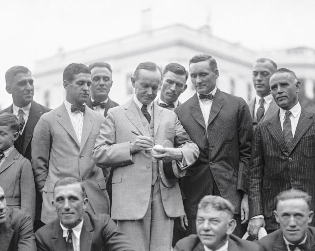 In this photograph, taken on September 5, 1924, President Calvin Coolidge signs a baseball for the Washington Senators baseball team during their visit to the White House. This visit followed their World Series championship during the baseball season of 1924. This was the first World Series win for a baseball team from Washington, D.C., and would remain the only such victory until the Washington Nationals became World Series champions in 2019.