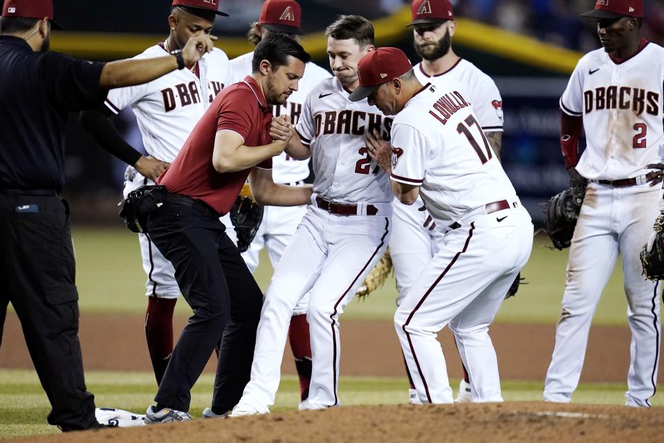 Arizona Diamondbacks starting pitcher Zach Davies, center, is helped up by Diamondbacks assistant athletic trainer Ryne Eubanks, front left, and manager Torey Lovullo (17) after being hit in the shin with a line drive by Kansas City Royals' Bobby Witt Jr. as Diamondbacks shortstop Geraldo Perdomo (2) and other teammates look on during the fourth inning of a baseball game Monday, May 23, 2022, in Phoenix. (AP Photo/Ross D. Franklin)