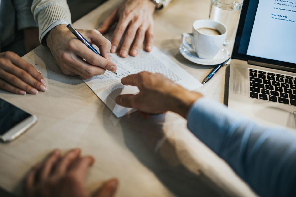 person signing document with tax accountant, laptop