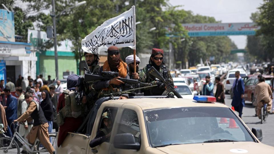 Schwer bewaffnete Taliban-Kämpfer patrouillieren mit wehender Flagge durch Kabul.