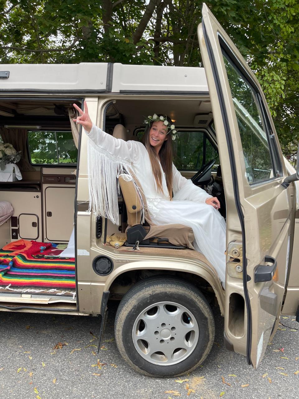 Kelly Anne Ferraro, wearing a wedding dress with a white fringe coat, sits in a van.