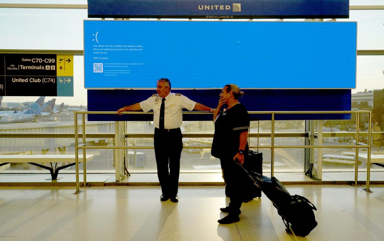 United Airlines employees at Newark International Airport wait by a departures screen displaying a "blue screen of death" last month