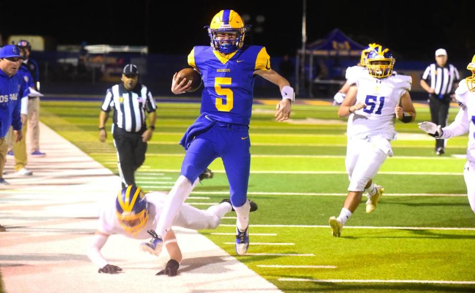 Dos Palos High School senior quarterback Peyton Van Worth (5) grimaces as he pulls up on the Broncos sideline after running the ball during a playoff game against Exeter on Friday, Nov. 17, 2023.