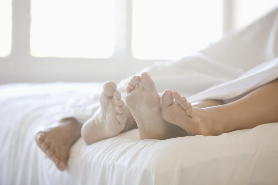 A couple's feet peek out from under white bed sheets, suggesting intimacy and closeness