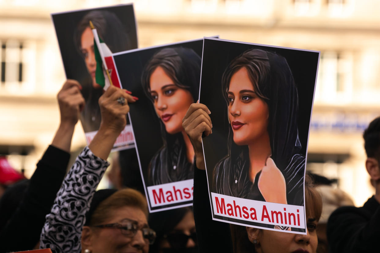 Protesters raise three identical pictures of Mahsa Amini.